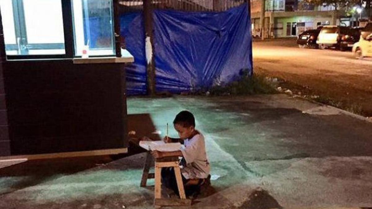 un baietel isi face temele in genunchi pe trotuar la lumina rece a neoanelor povestea lui a devenit