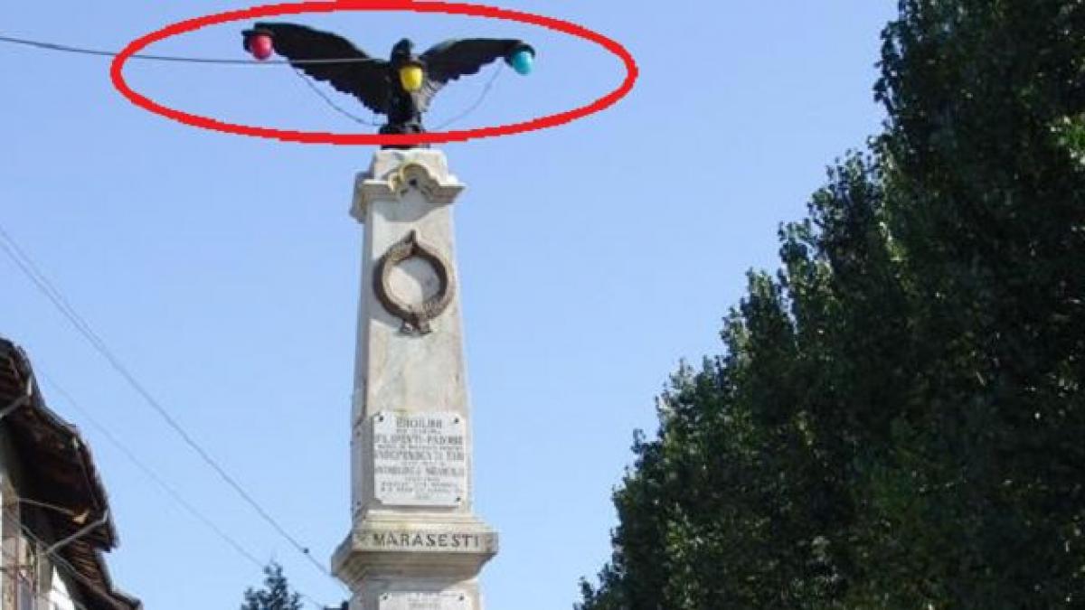 un vultur cu bec in cioc un monument ridicat in memoria eroilor decorat cu lampi de iluminat public