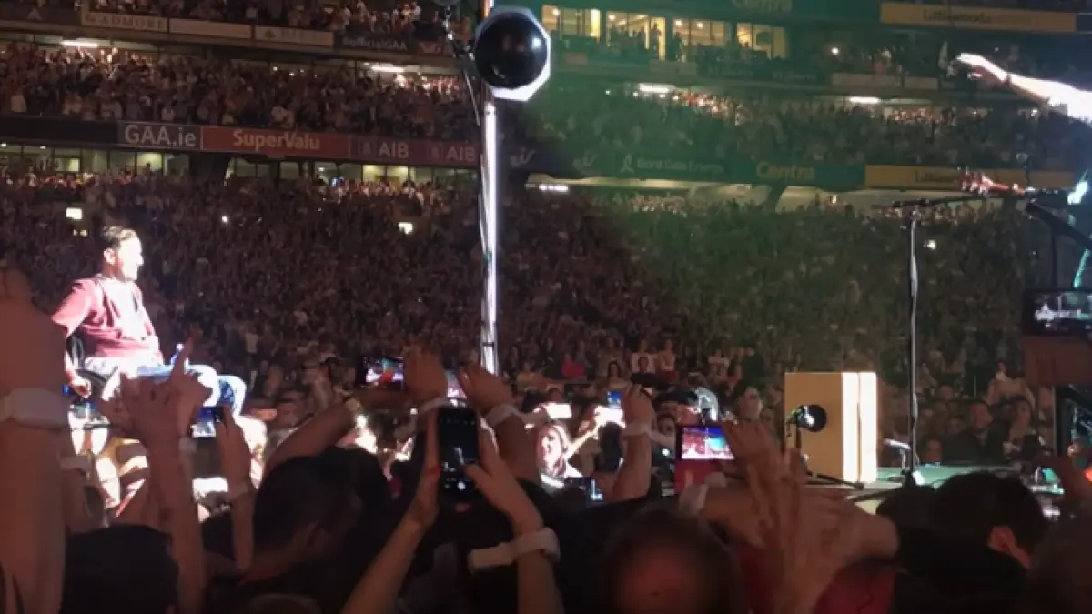 fan coldplay in scaun cu rotile purtat pe brate de multime pana pe scena