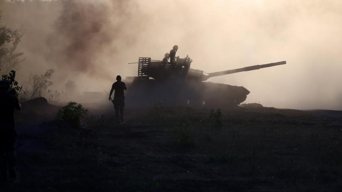Tanc intr-un nor de praf si fum in timp ce un militar cu arma mana merge in fata acestuia