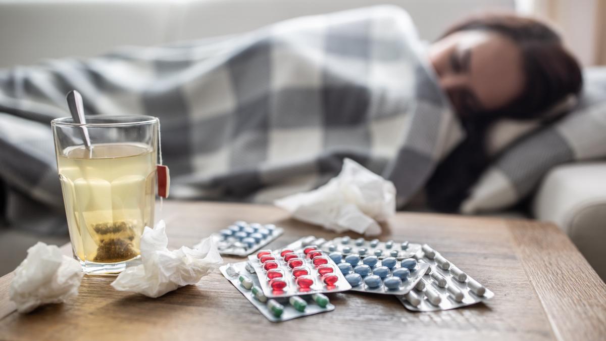 femeie invelita pe canapea cu medicamente si ceai langa ea