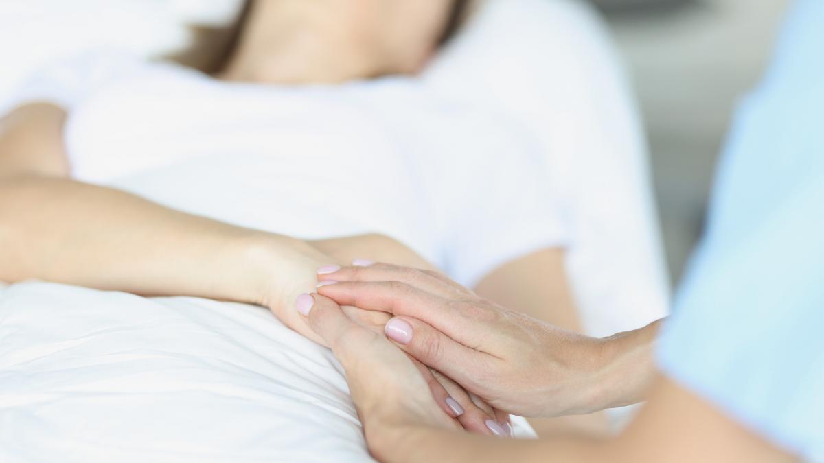 O femei tine de mana o alta persoana care se afla pe patul de spital