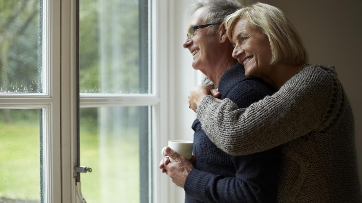 cuplu in varsta, se strang in brate si privesc pe geam 