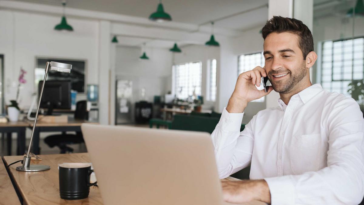 barbat care lucreaza pe laptop si vorbeste la telefon