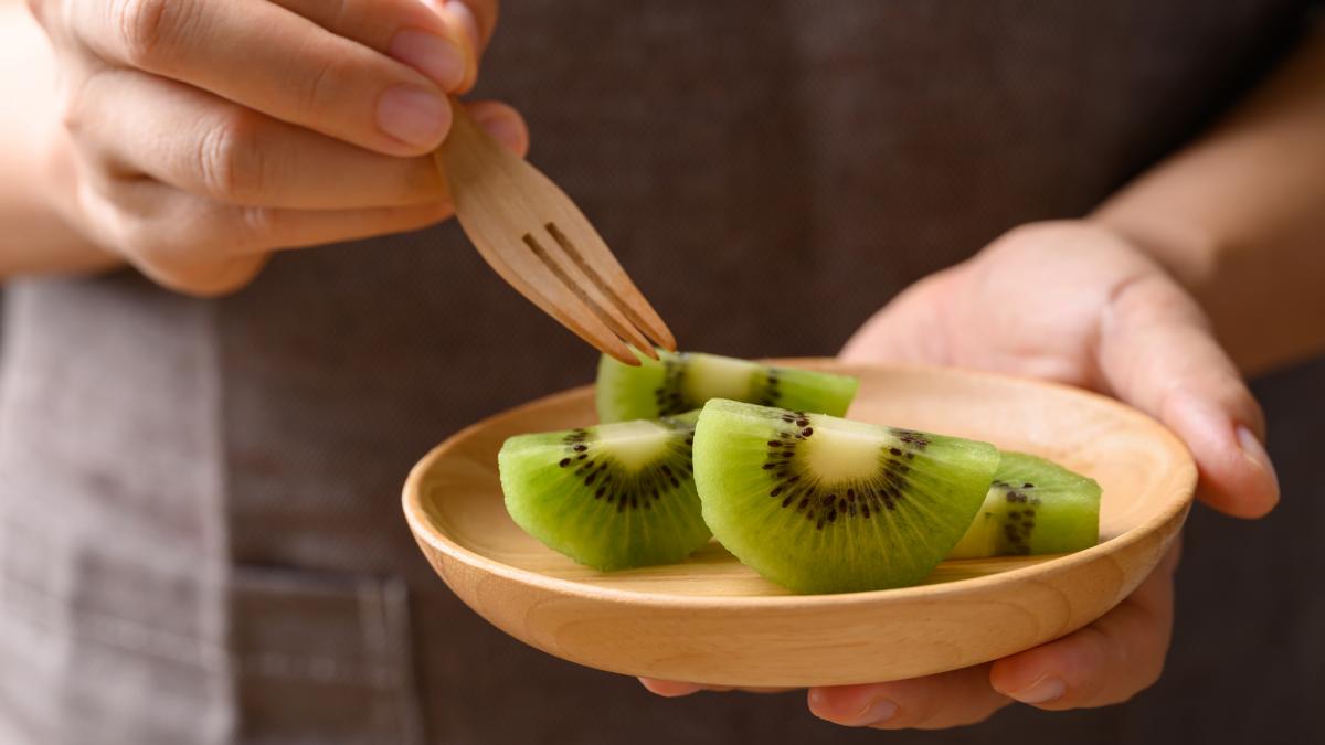 un barbat ia cu o furculita o bucate de kiwi dintr-o farfurie