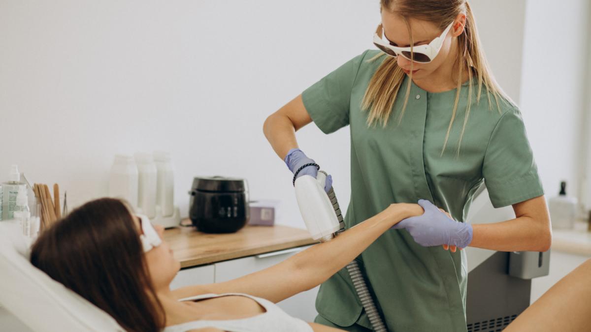 Tehnician epilare şi clientă în timpul unei proceduri de epilare definitivă în salon