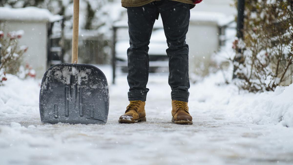 barbat care sta cu lopata in mana pe un trotuar acoperit de gheata