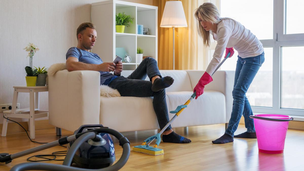 femeie care face curat si barbat care sta pe telefon getty images