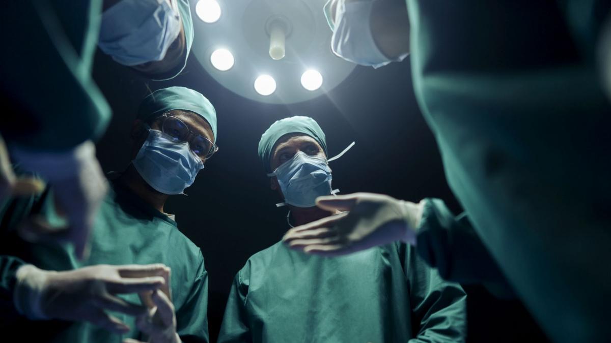 patru medici chirurgi care se sfatuiesc in sala de operatie