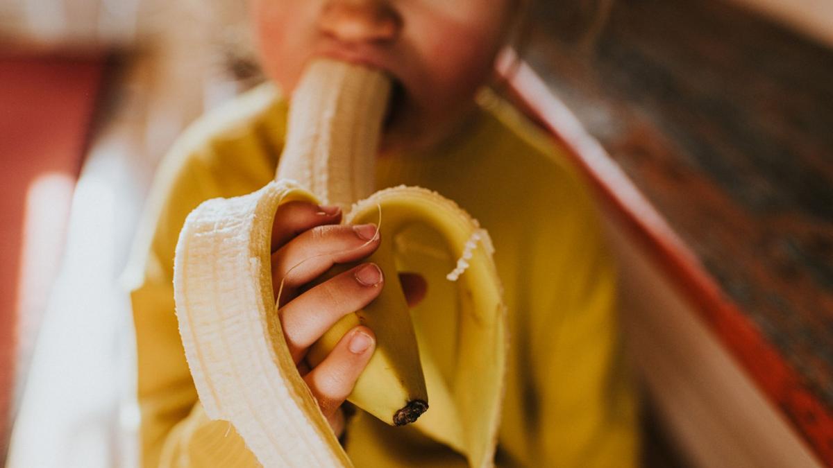 copil imbracat cu o bluza galbena care musca dintr-o banana