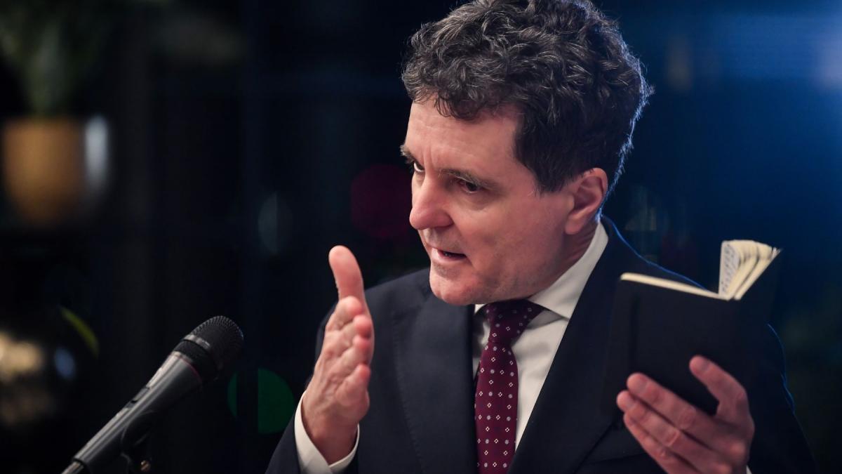 presedintele nicusor dan intr-o conferinta de presa tinand o agenda in mana in timp ce vorbeste