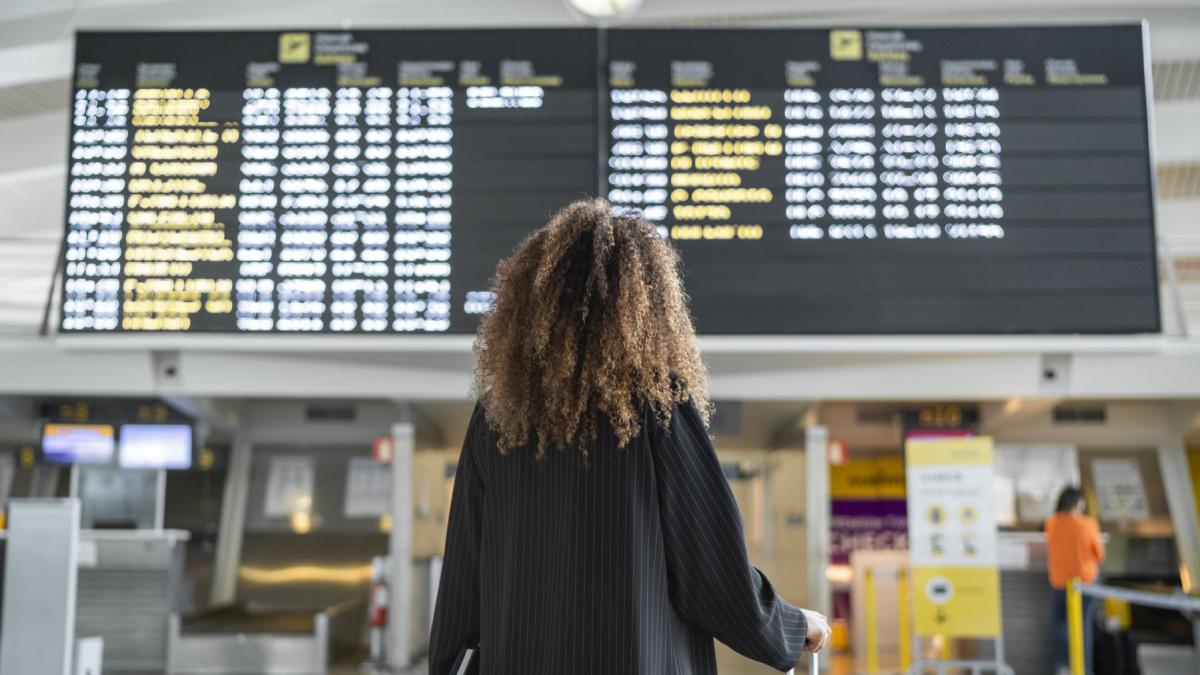 femeie cu trollerul in mana care se uita pe panoul plecari in aeoport