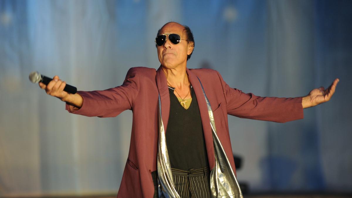 Adriano Celentano pe scena cu un microfon in mana si cu mainile deschise