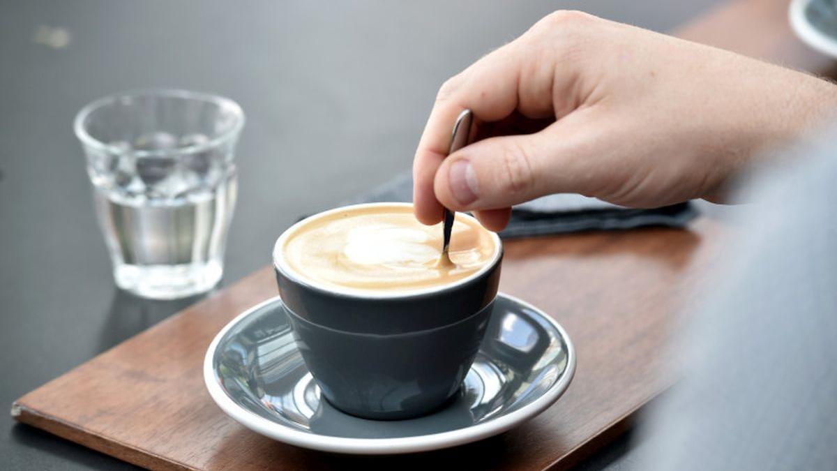 barbat care amesteca in ceasca de cafea si are un pahar de apa langa