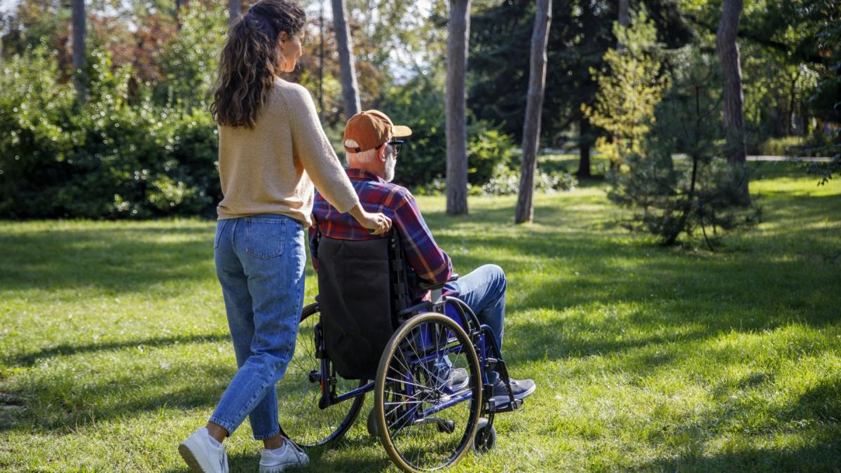 femeie care impinge un barbat in carucior cu rotile