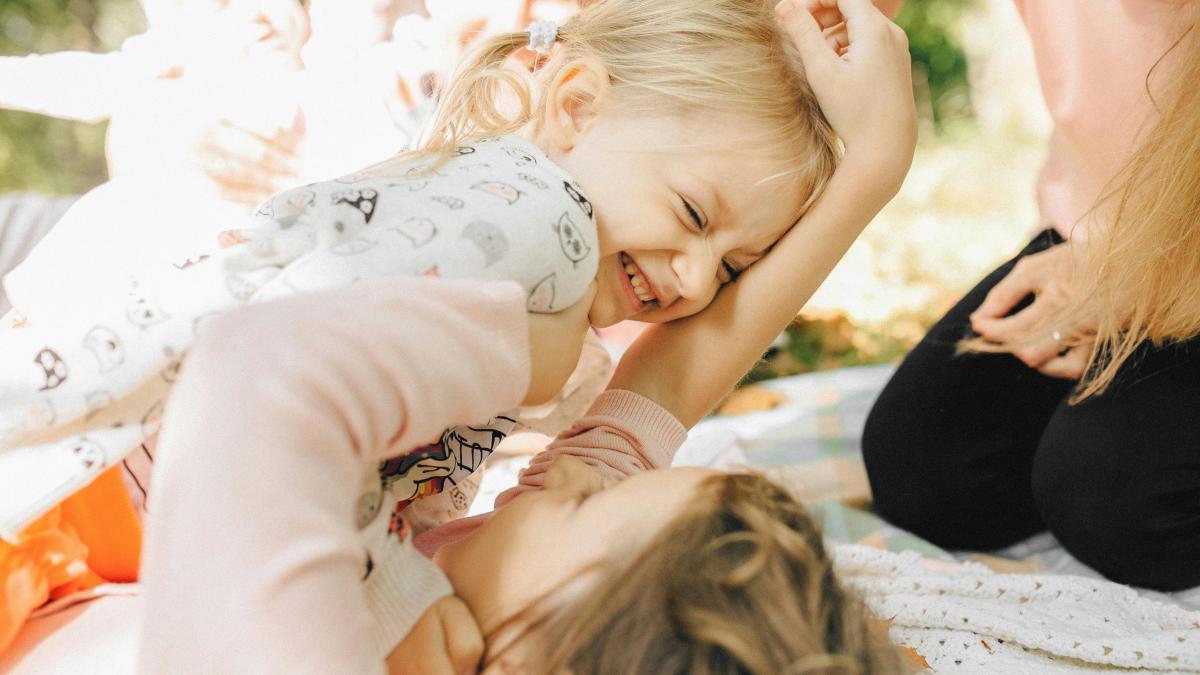 doua fetite fericite se joaca pe o paturica