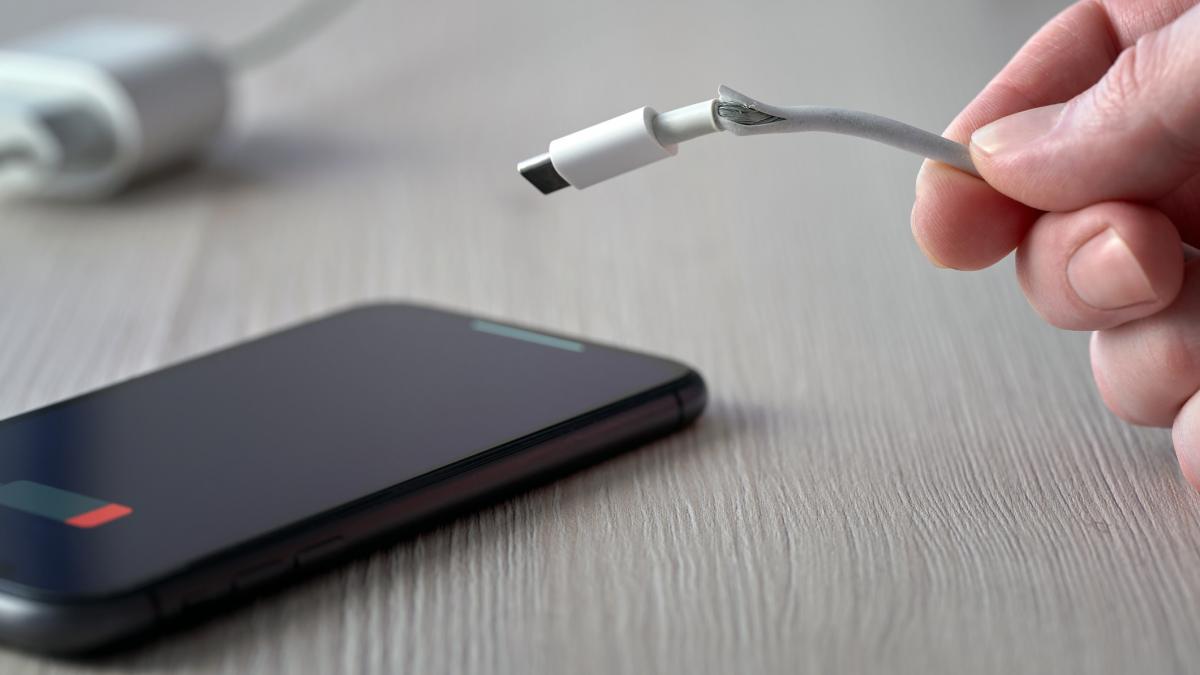 barbat care tine in mana un incarcator rupt si un telefon descarcat pe masa