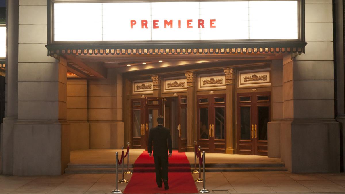 barbat la costum in fata unui cinema pe care scrie premiera