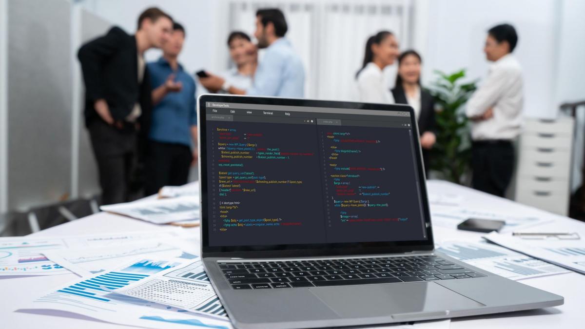 un laptop cu cod de programare si angajati it pe fundal