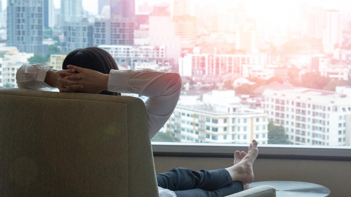 o femeie se relaxeaza stand in fotoliu si uitandu-se la privelistea orasului care se vede prin fereastra