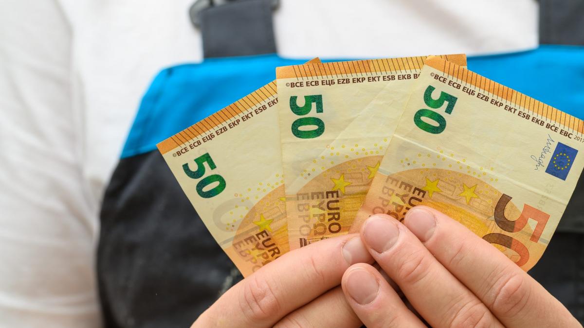 muncitor care tine trei bancnote de 50 de euro in mana