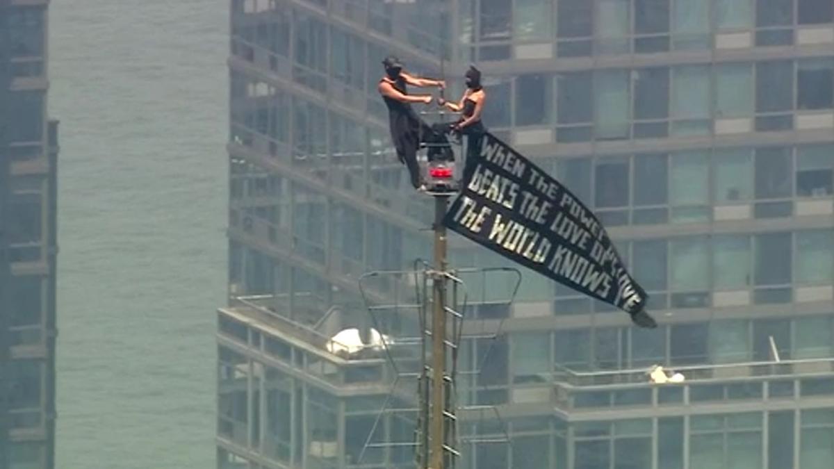 doi mascati au urcat pe catargul de pe empire state building si au desfasurat un banner apoi unul dintre ei a facut un gest uluitor