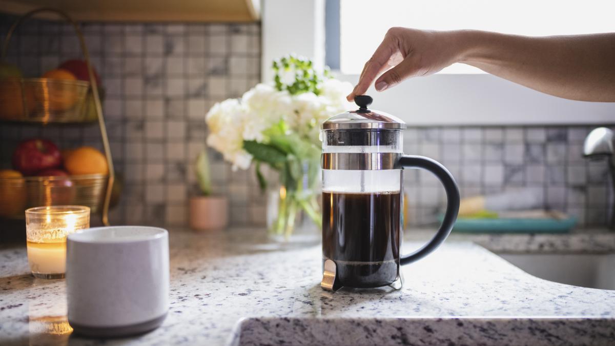 poza in care apare un ibric cu cafea facuta si mana unei femei care se pregateste sa il foloseasca