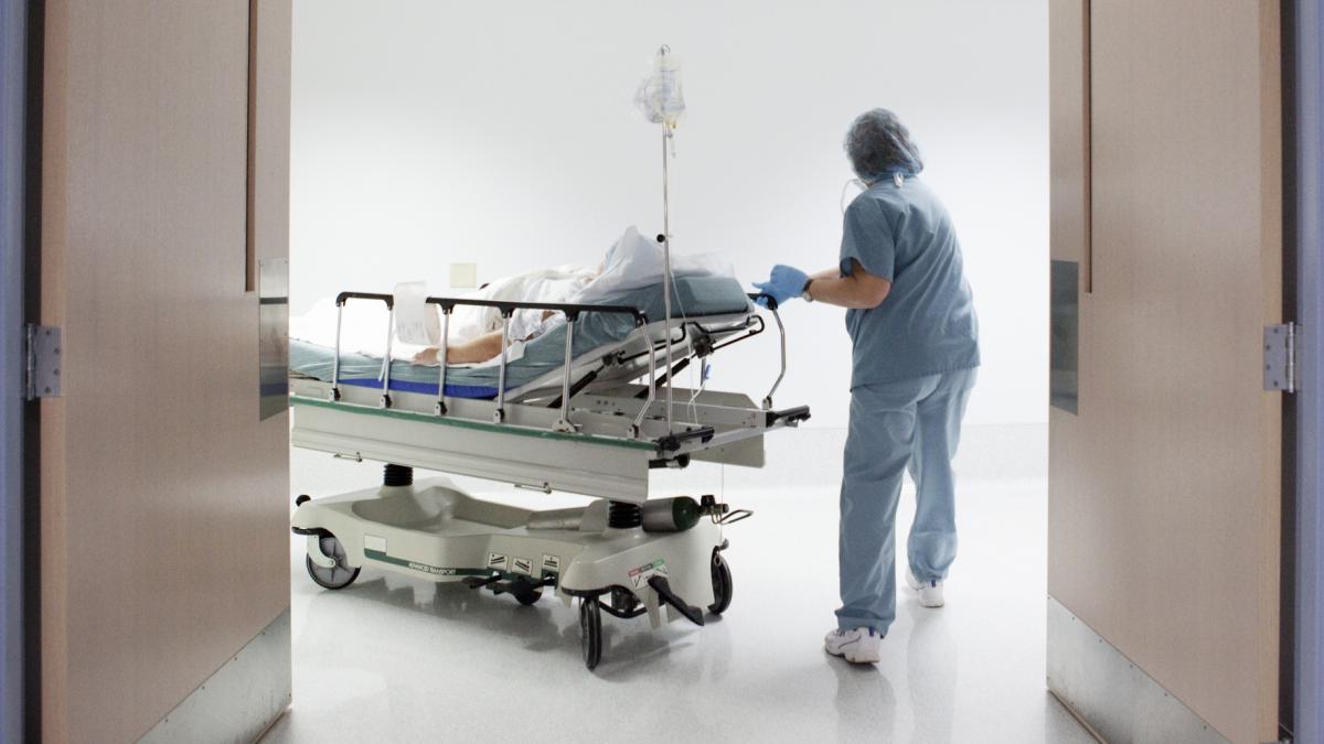 poza dintr-un spital in care apare o asistenta care transporta pe un pat mobil un pacient