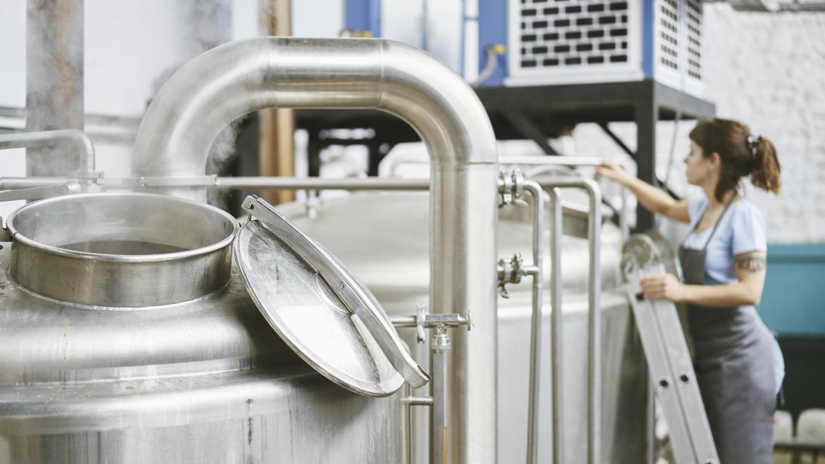 Rezervoare-industriale-din-inox-cu-un-operator-care-verifică-echipamentele-tehnologice