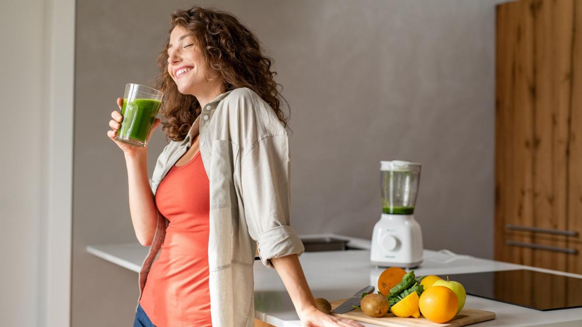 femeie fericita in bucătărie cu un smoothie verde in mana
