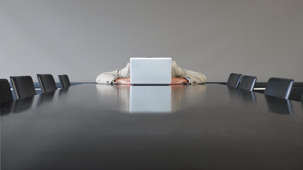 barbat cu capul in laptop la un birou cu scaune goale