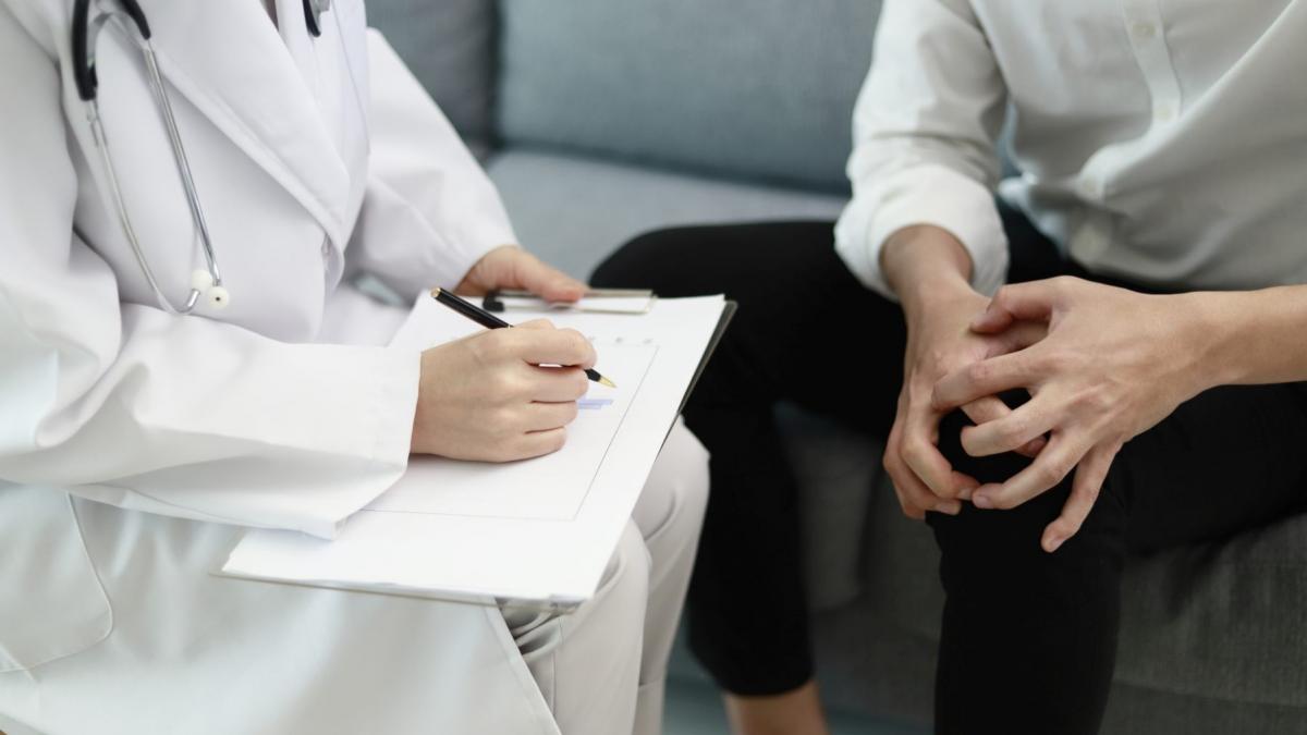 doctor care scrie o fisa cu pacientul care ii arata zona genunchiului