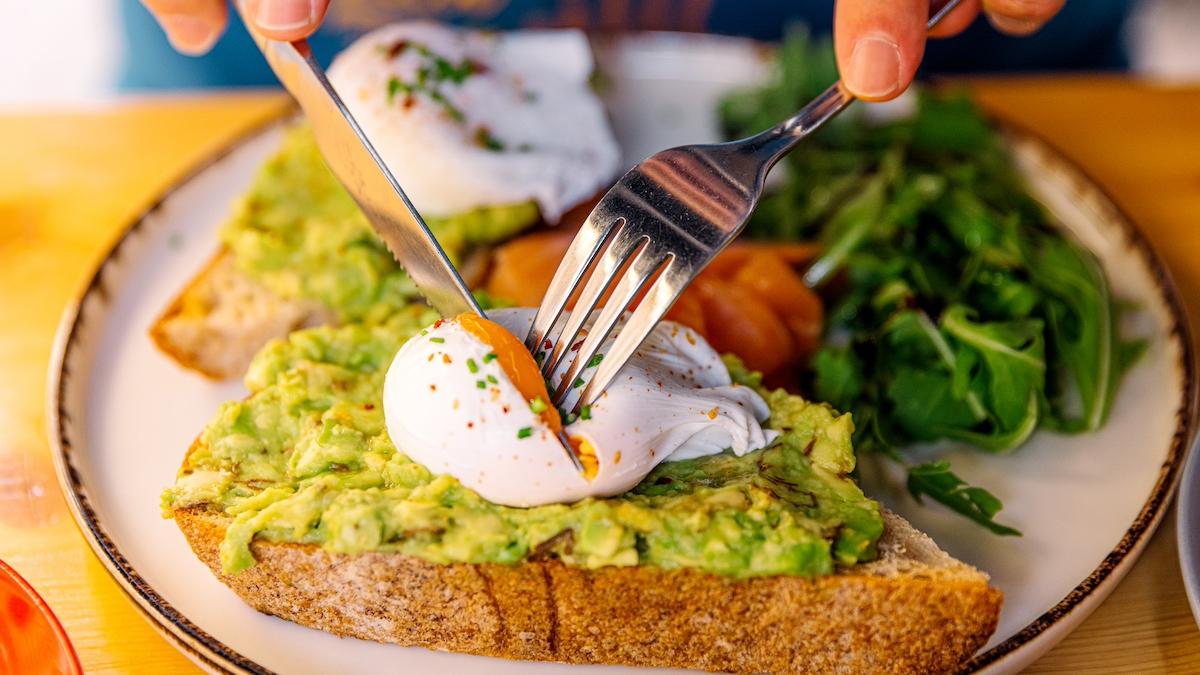 toast cu avocado și ou posat deasupra taiat de un cutit si o furculita