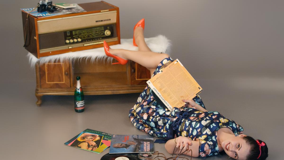 o femeie întinsă pe jos cu o carte in mana si cu picioarele pe o masa cu un radio pe ea
