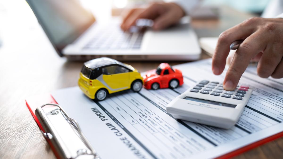 barbat care calculeaza pe calculator cu documente in fata si doua masinute