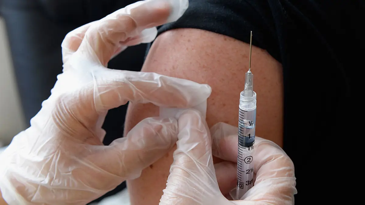 doua maini cu manusi care pun un plasture pe un brat dupa vaccin