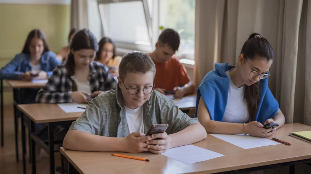 mai multi elevi stau in banca si se uita in telefoane