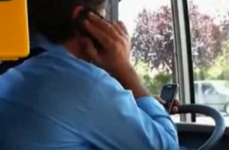 Un şofer de autobuz conduce vorbind la un telefon şi configurând e-mailul pe un altul 