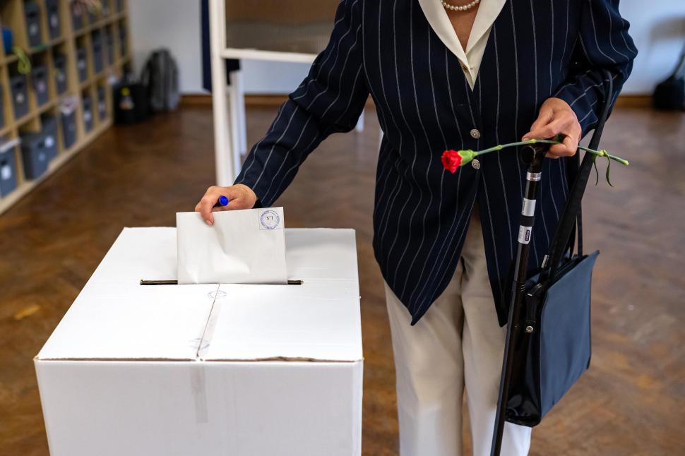 Femeie cu cămaşă neagră şi o floare roşie în mână pune un buletin de vot în urnă.