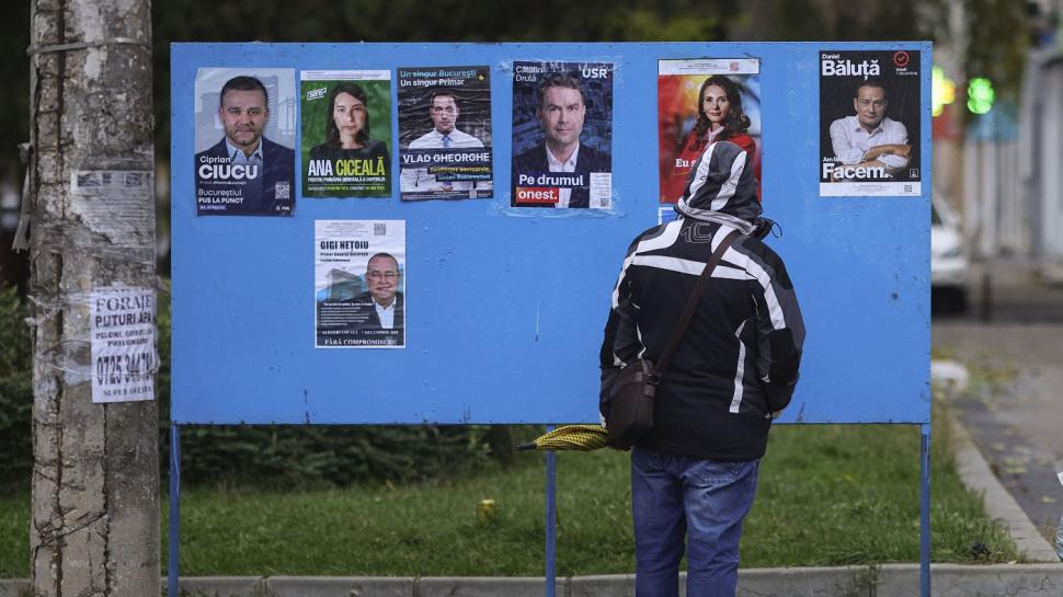 un barbat cu gluga pe cap s-a oprit în fata unui panou cu afise electrorale