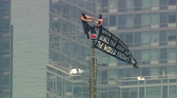 doi mascati au urcat pe catargul de pe empire state building si au desfasurat un banner apoi unul dintre ei a facut un gest uluitor