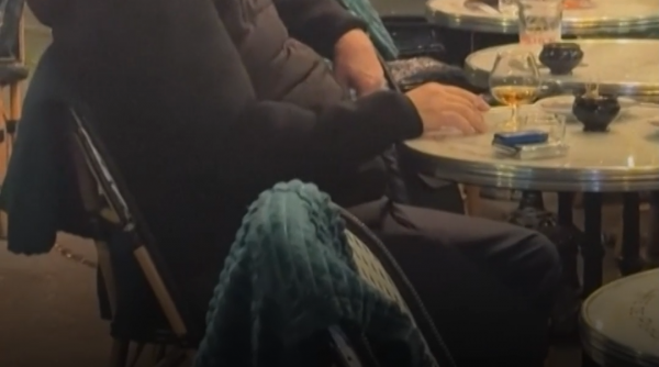 Un cuplu de francezi bea vin și savurează relaxat o țigară la o terasă, în timp ce, lângă ei, Parisul arde