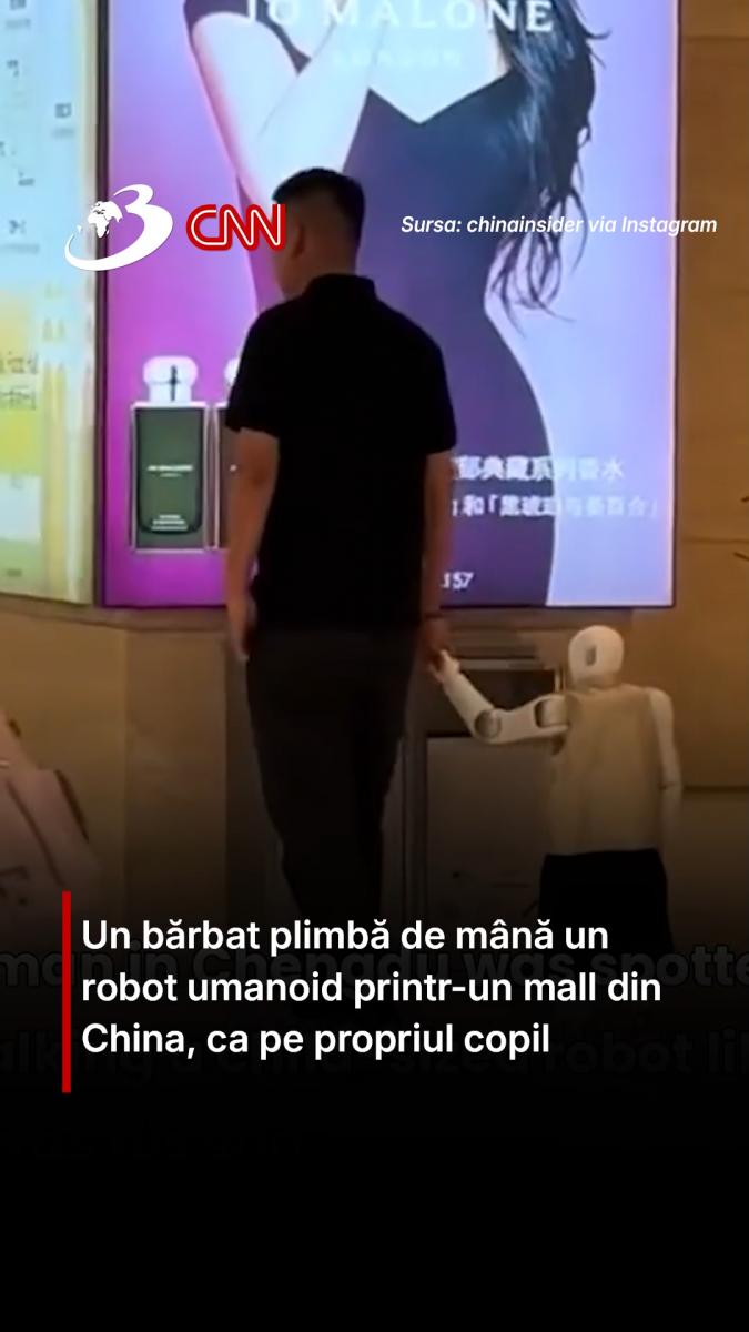 Un bărbat plimbă de mână un robot umanoid printr-un mall din China, ca pe propriul copil